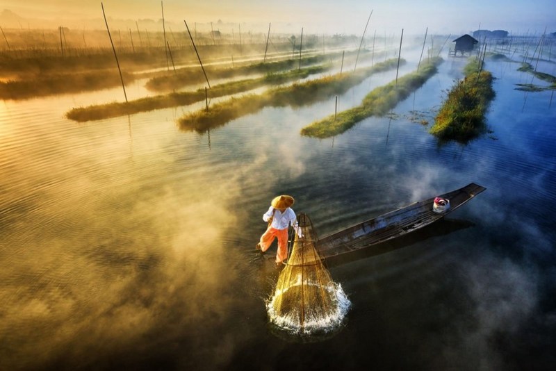 "Một ngư dân Intha đang tung lưới đánh cá khi đang đứng trên thuyền với kỹ thuật chèo chân độc đáo ở Hồ Inle của Myanmar".